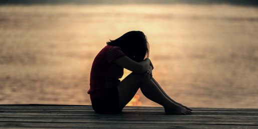 A person sitting on a dock at sunset with their knees pulled up to their head.