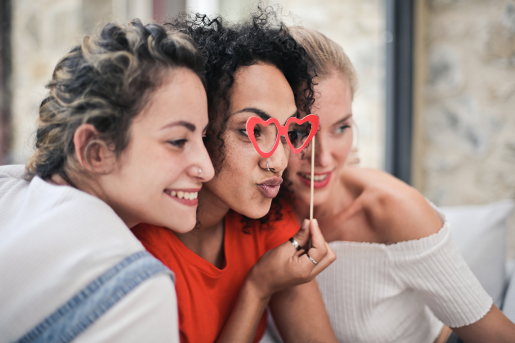 Three adults posing together for a selfie. One has a pair of novelty heart-shaped glasses for a silly pose.