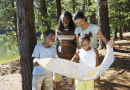 A family looks at a large paper map together while walking through the woods.