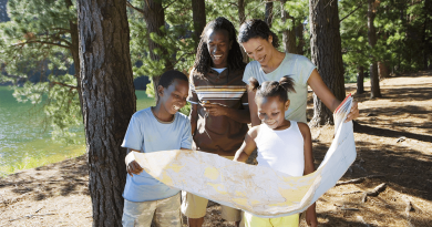 A family looks at a large paper map together while walking through the woods.