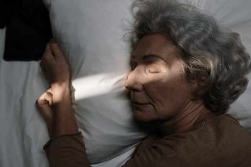 An older adult asleep in bed. A ray of light goes across her face and arm.