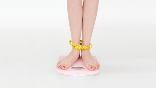 A person standing on a scale with a measuring tape wrapped around their ankles.