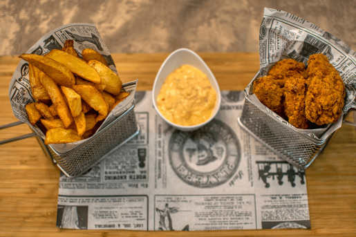 Fried chicken tenders and potato wedges in serving cups along with a yellow sauce.