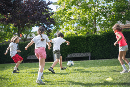 A group of children kicking a soccerr ball on a bright, sunny day.