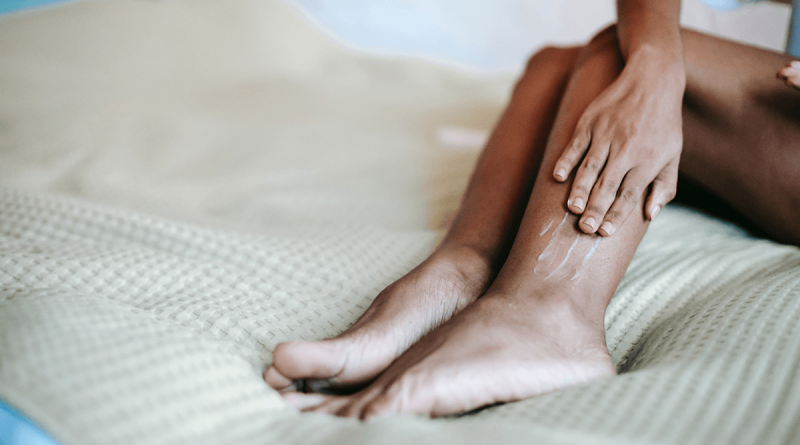 A person laying on a bed, rubbing their calf.