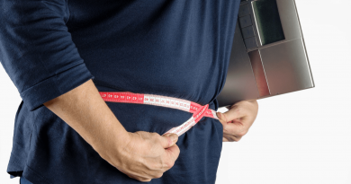 A person with a measuring tape wrapped around their waist while holding a scale.