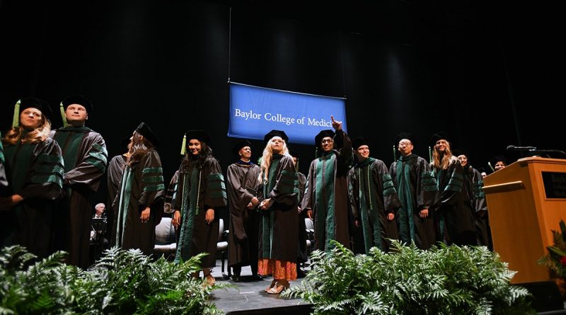 A graduating class dressed in black and green robes standing on the stage.