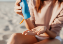 A person sitting on the beach squeezing sunscreen into their hand.
