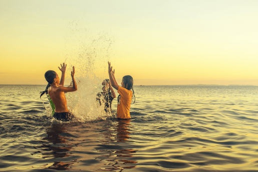 Four children playing in the ocean near sunset.