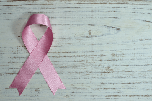 A pink breast cancer ribbon laying on a wooden table