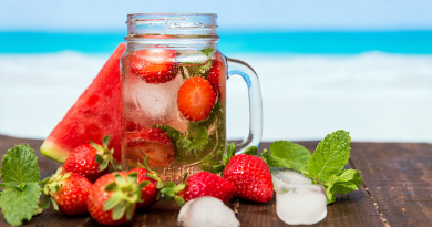 A glass filled with fruits like strawberry and watermelon on a table by the ocean.