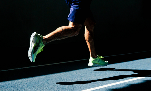 A person seen from behind, jogging on a dark track.