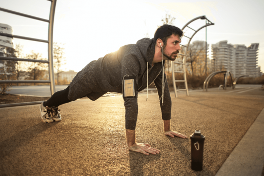 A person in the "up" position while doing pushups in a park with the sun rising behind them.