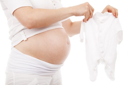 A pregnant person wearing all white holding a white baby onesie.