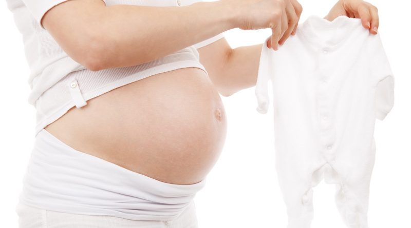 A pregnant person wearing all white holding a white baby onesie.
