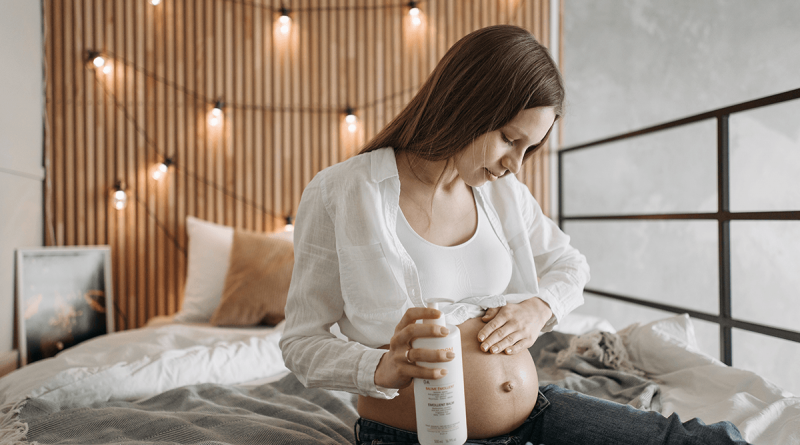 A pregnant person rubbing a skin product into their stomach.