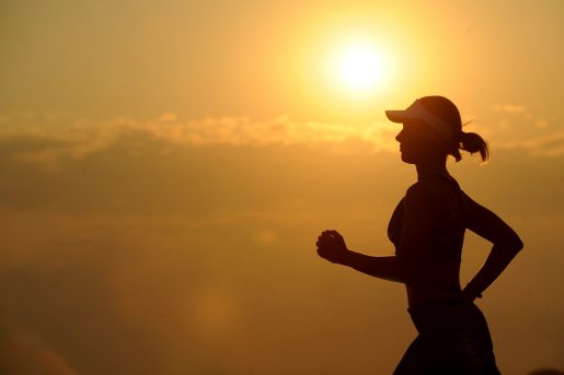 A person jogging at sunset, their body a silhouette in front of an orange sky and sun