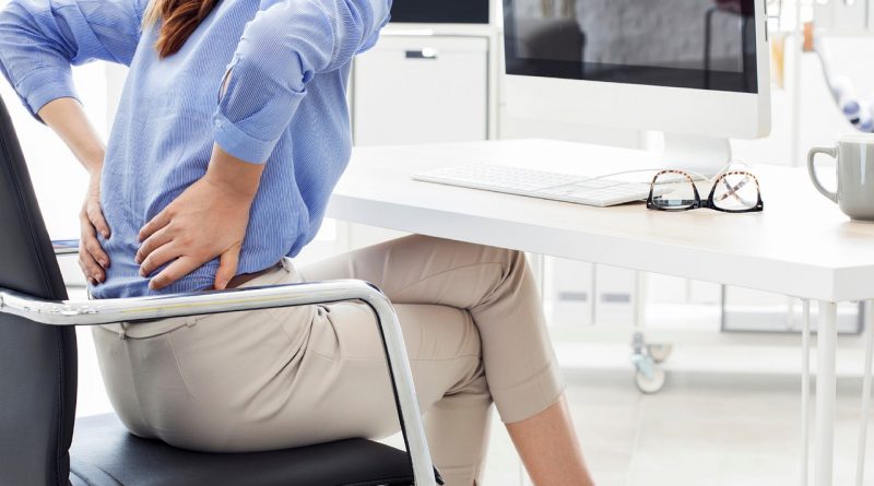 A person sitting at a desk while clutching their back in pain.