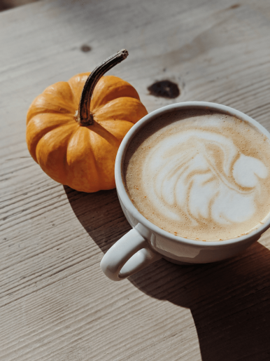 A miniature pumpkin to the left of a filled coffee mug.