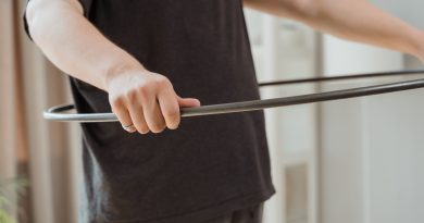 A person holding a black hula hoop at waist level.