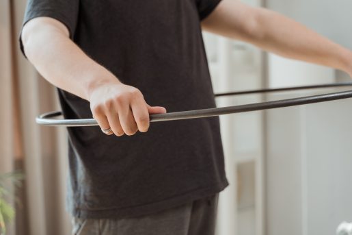 A person holding a black hula hoop at waist level.