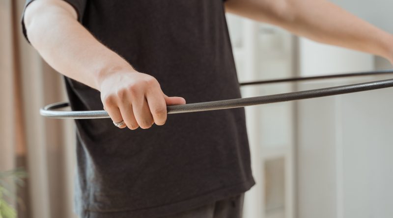 A person holding a black hula hoop at waist level.