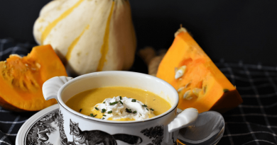 A bowl of brightly-colored pumpkin soup on a table with some raw pumpkin.