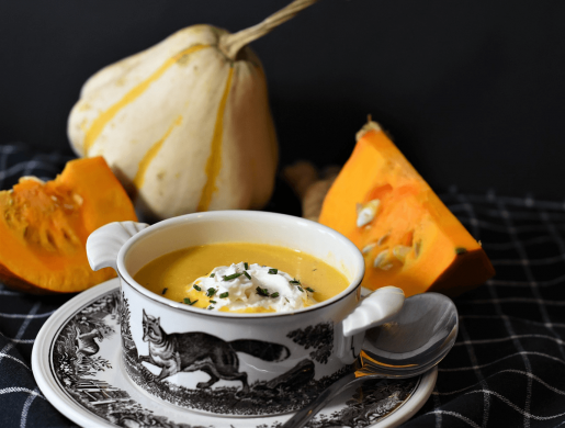 A bowl of brightly-colored pumpkin soup on a table with some raw pumpkin.