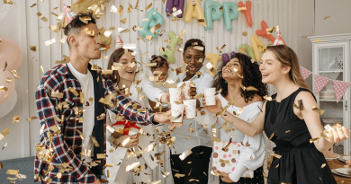 A group celebrating by raising glasses to each other while golden confetti rains down on them.