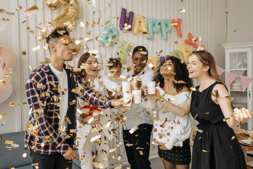 A group celebrating by raising glasses to each other while golden confetti rains down on them.