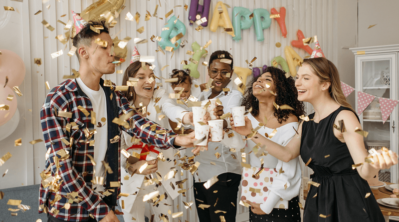 A group celebrating by raising glasses to each other while golden confetti rains down on them.