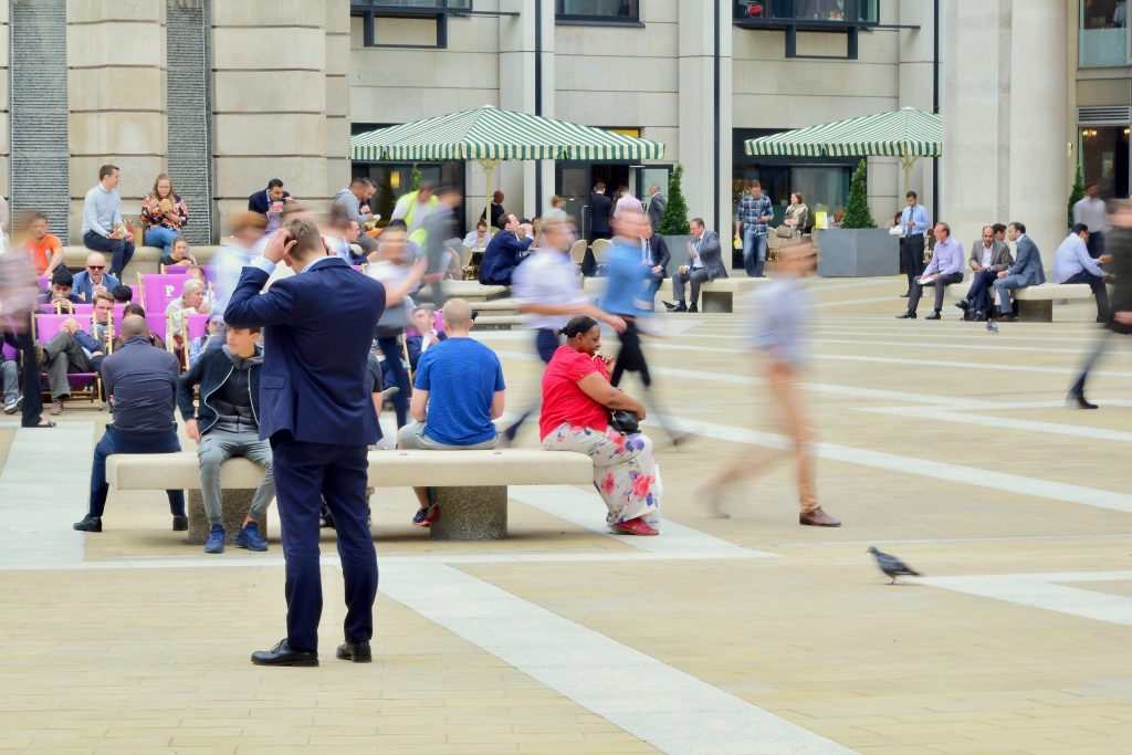 A crowd rushing around a person seated on a bench outside.