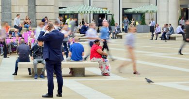 A crowd rushing around a person seated on a bench outside.