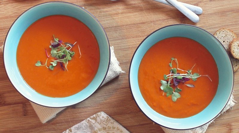 Two brightly colored red soups with fresh greens garnishing the top.