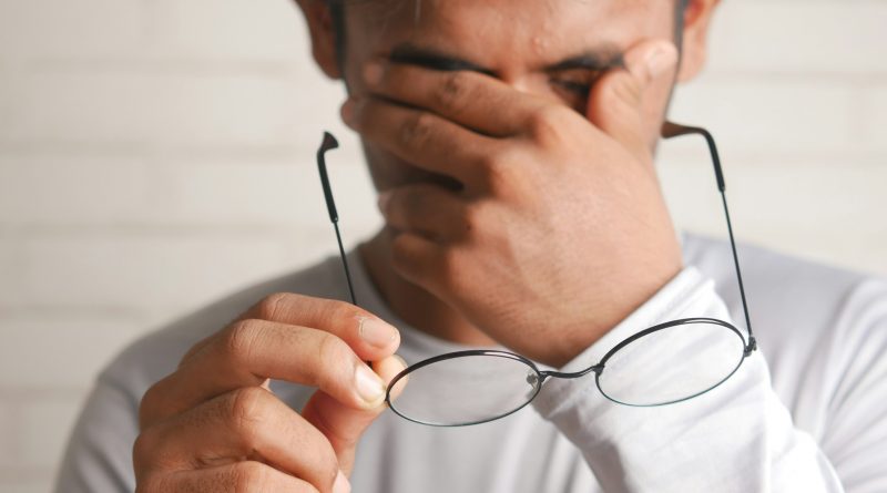 A man rubbing his eyes and holding his glasses