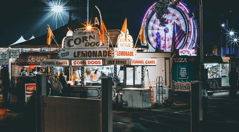 A brightly-lit corn dog stand at a carnival at night.
