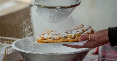 A funnel cake being sprinkled with powdered sugar.
