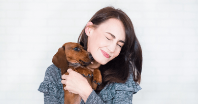 A person scrunching up their face as a Dachshund they're holding licks them