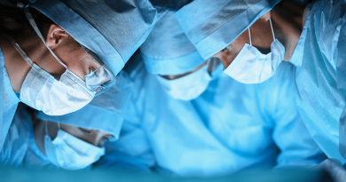 Four surgeons in blue scrubs looking down on a surgery table.