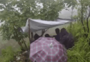 Clinicians huddled together in a rainy forest under a makeshift tent.