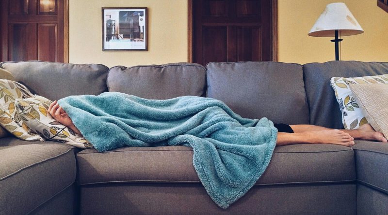 A person laying under a blanket on a couch.