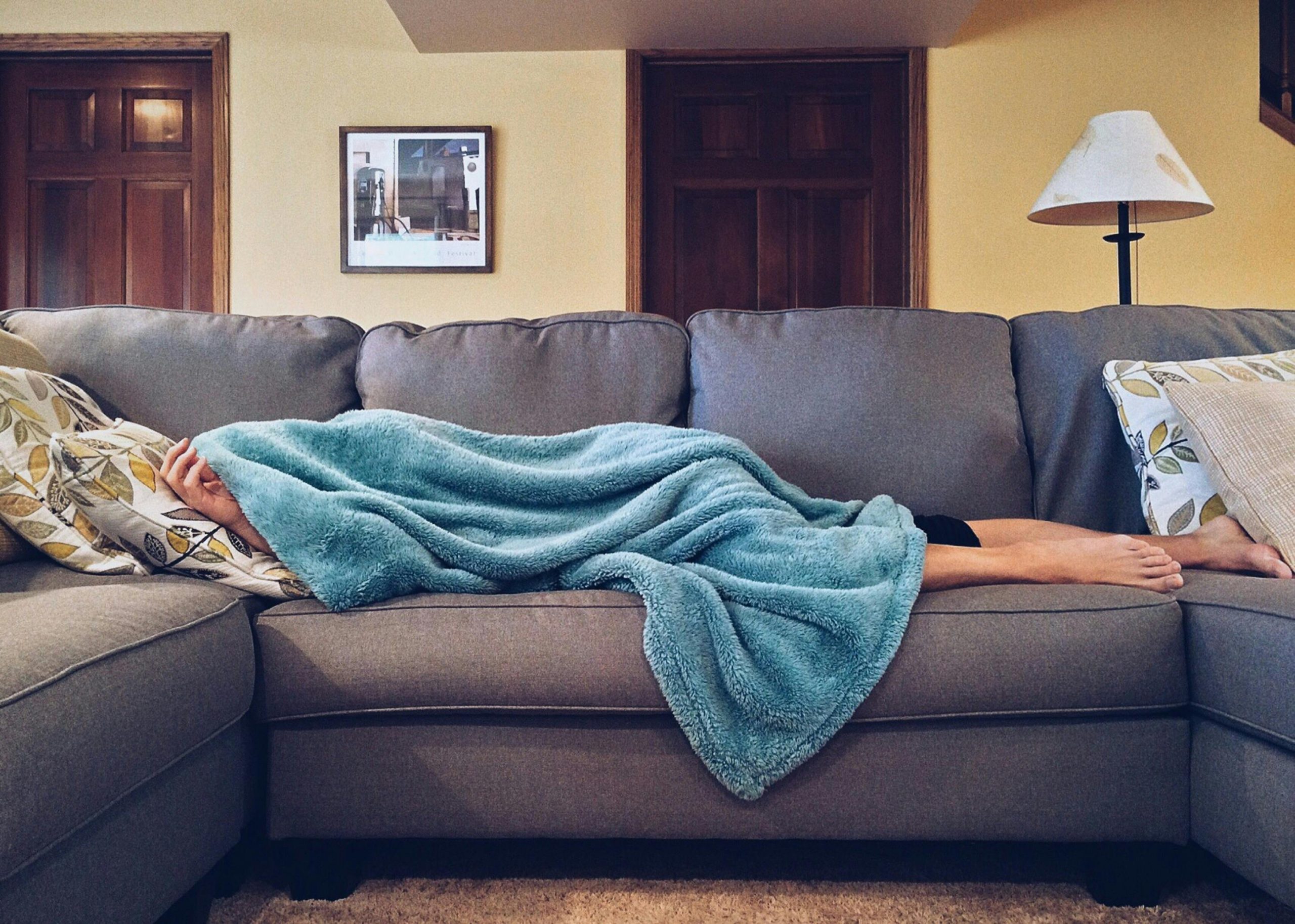 A person laying under a blanket on a couch. Only feet and a hand are visible.