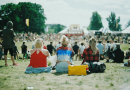 Three friends sitting in a field overlooking an outdoor festival.