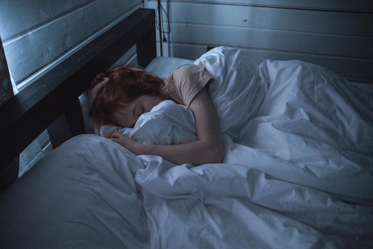 A person in a dark room sleeping with a blanket pulled tight around them.