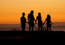 Two adults and two children stand looking out at ocean during sunset.