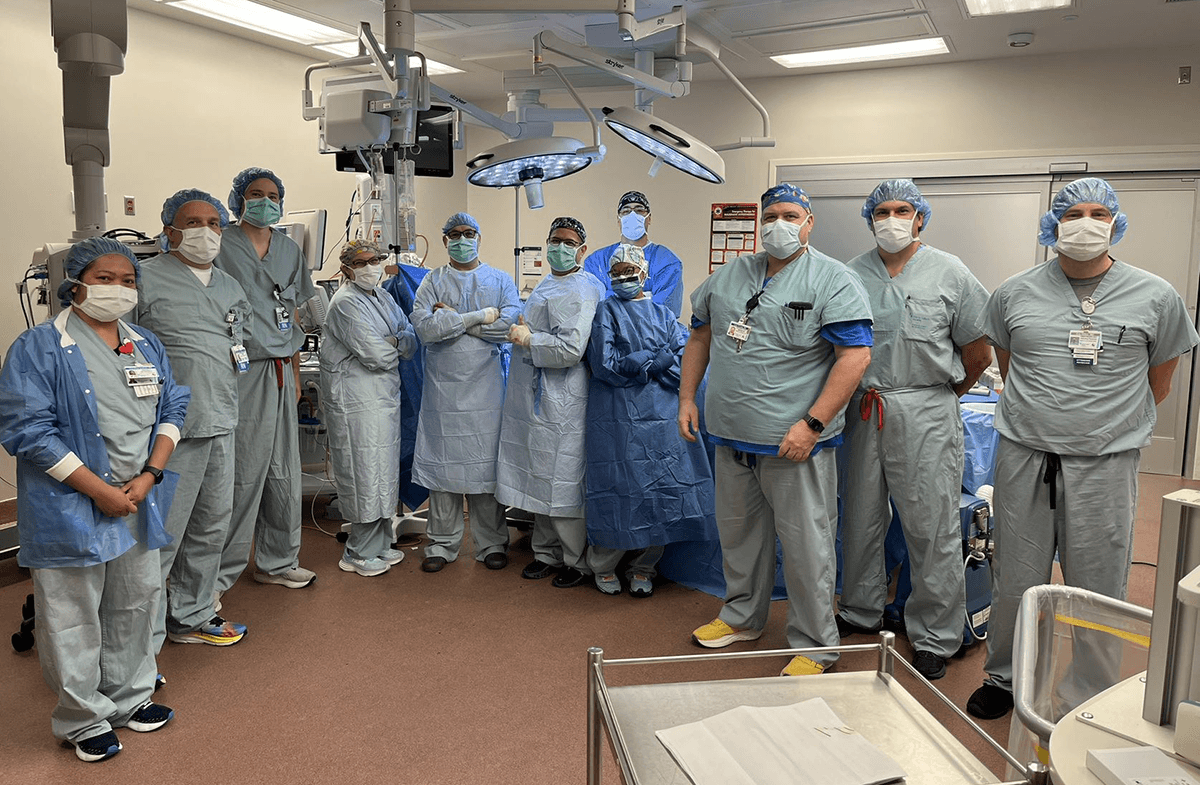A large group of doctors wearing surgical scrubs posing in a surgery room.
