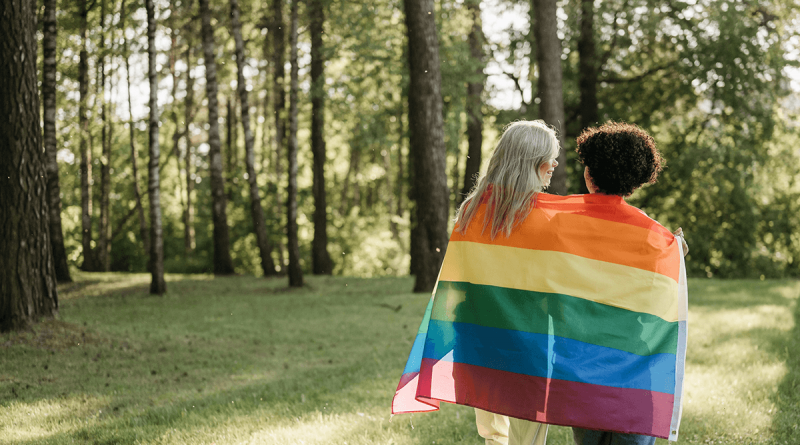 A pair of older adults walking through the woods, wrapped closely together in a Pride flag