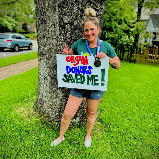 A person outside holding a sign that reads "Organ donors saved me!"