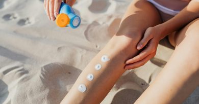 A person massaging sunscreen onto their legs on a sandy beach.