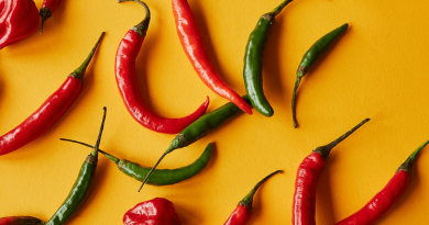 A collection of vibrant red and green chili peppers set on a yellow surface.